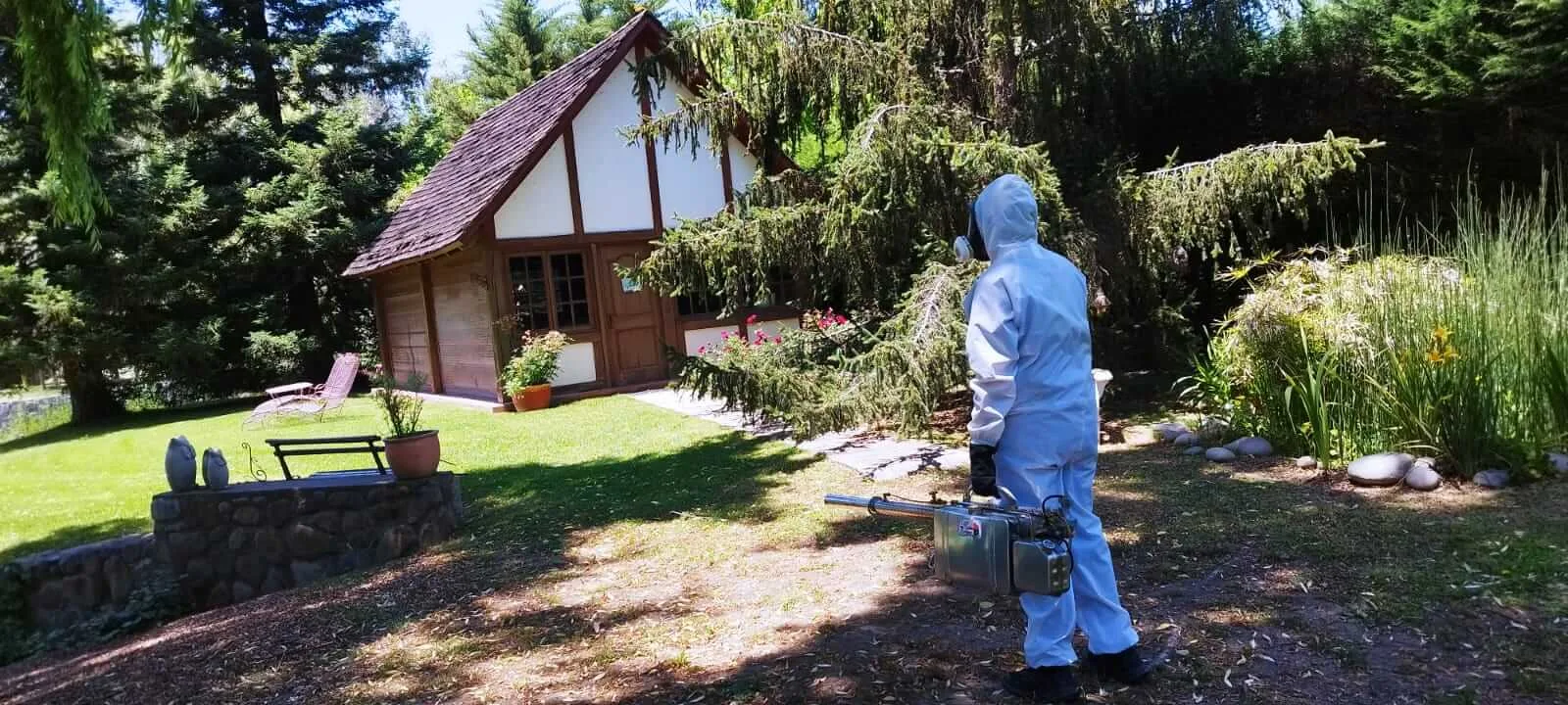 Técnico con traje azul de protección fumigando el exterior de una vivienda con jardín en Santiago